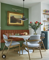 An oval white Carrara marble dining table with a tulip style aluminum stem base, placed on a white floor, with chairs around it and a vase with flowers on the table.