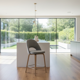 A gray upholstered Saarinen style executive counter stool with a metal footrest, featuring a cushioned seat and backrest, supported by a wooden stool with a circular shape.