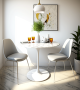 A round marble dining table with a white gloss base, surrounded by two chairs, set in a well-lit room with a decorative wall painting above.