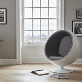 Modern white chair with gray cushion in a room with large windows and framed pictures on the wall.