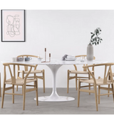 An oval Italian marble tulip dining table with a bevelled edge, placed in a room with a green wall, a framed picture on the wall, and modern furniture.